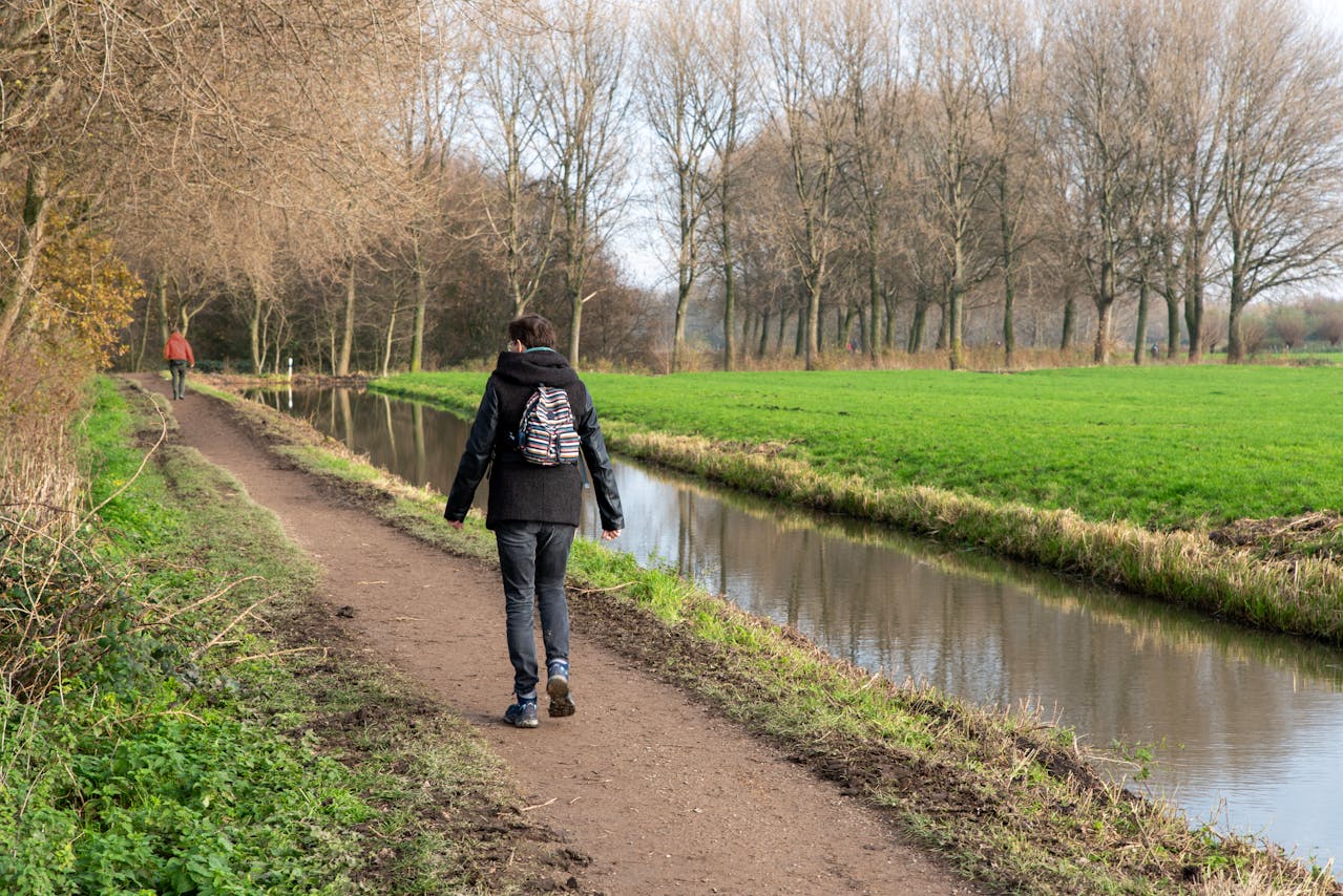 Pieterpad, twee mensen wandelen op een rustig pad langs de rivier, omringd door de natuur in het vroege voorjaar.